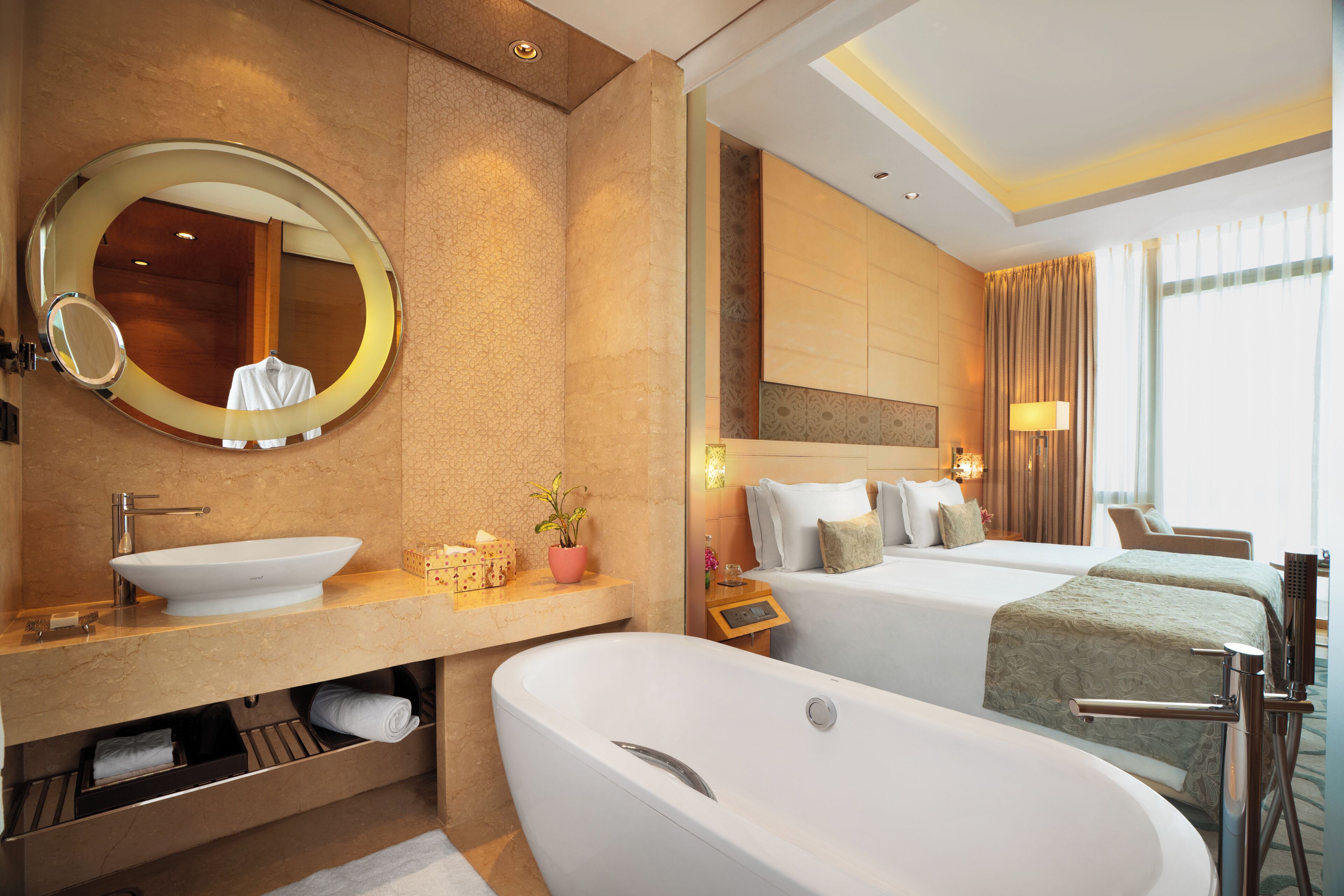 Une chambre d’hôtel moderne dotée d’une grande baignoire, d’un miroir rond, d’une coiffeuse avec un lavabo et de deux lits offrant une vue sur la ville.