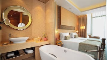 Une chambre d’hôtel moderne dotée d’une grande baignoire, d’un miroir rond, d’une coiffeuse avec un lavabo et de deux lits offrant une vue sur la ville.