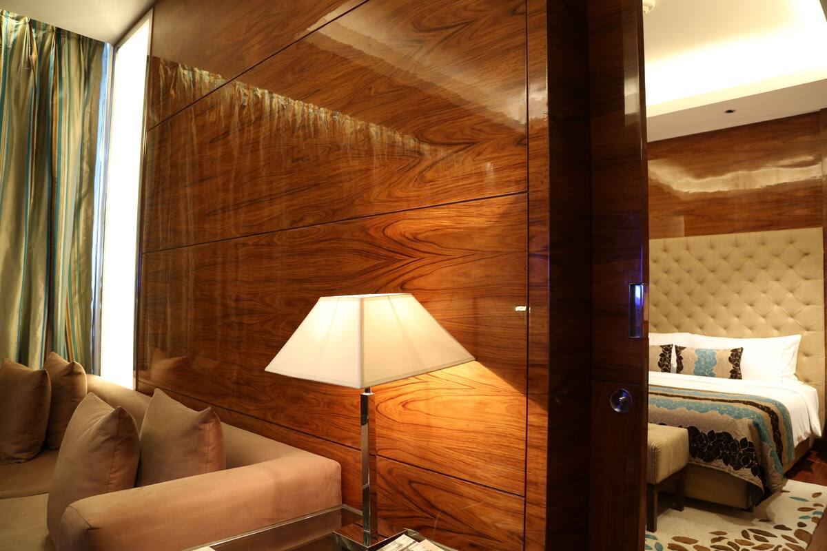 A hotel room with a wooden panel wall, a sofa, a bedside table with a lamp, and a bed with a tufted headboard.