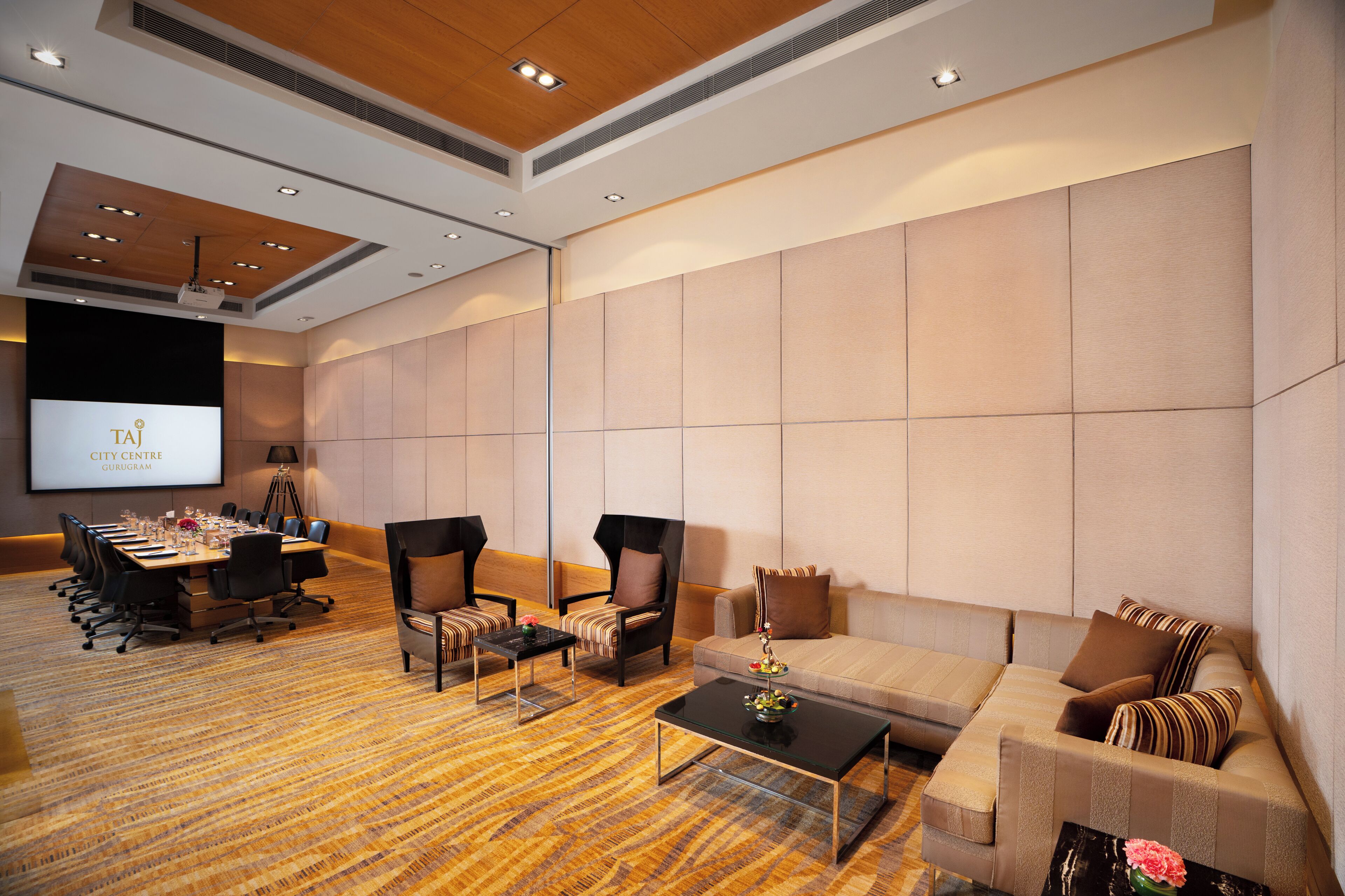 A conference room with a large screen, a long table with chairs, a sofa, and a coffee table.