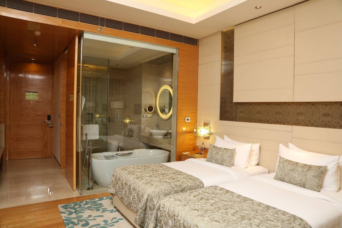 A hotel room with a large bed, a separate bathroom with a bathtub, and a sliding glass door leading to a shower area.