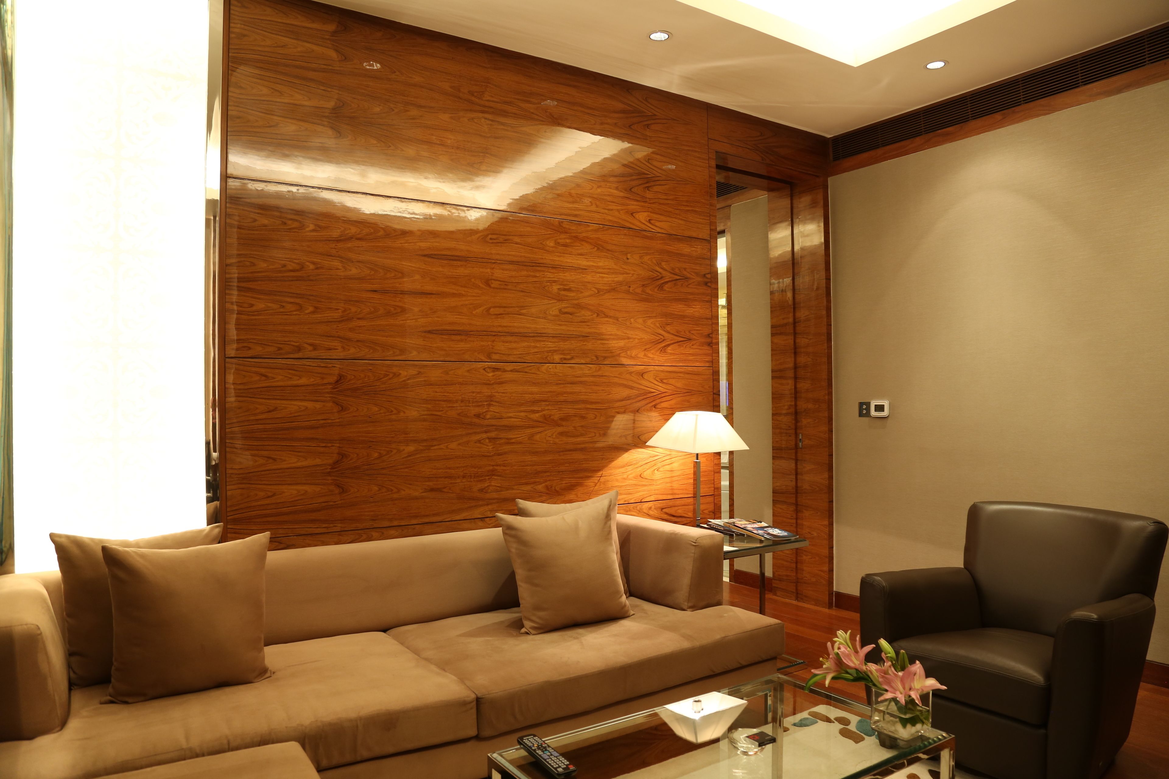 Una habitación de hotel moderna con una pared decorativa de madera, un sillón de cuero, una mesa de centro de vidrio y un sofá con cojines.