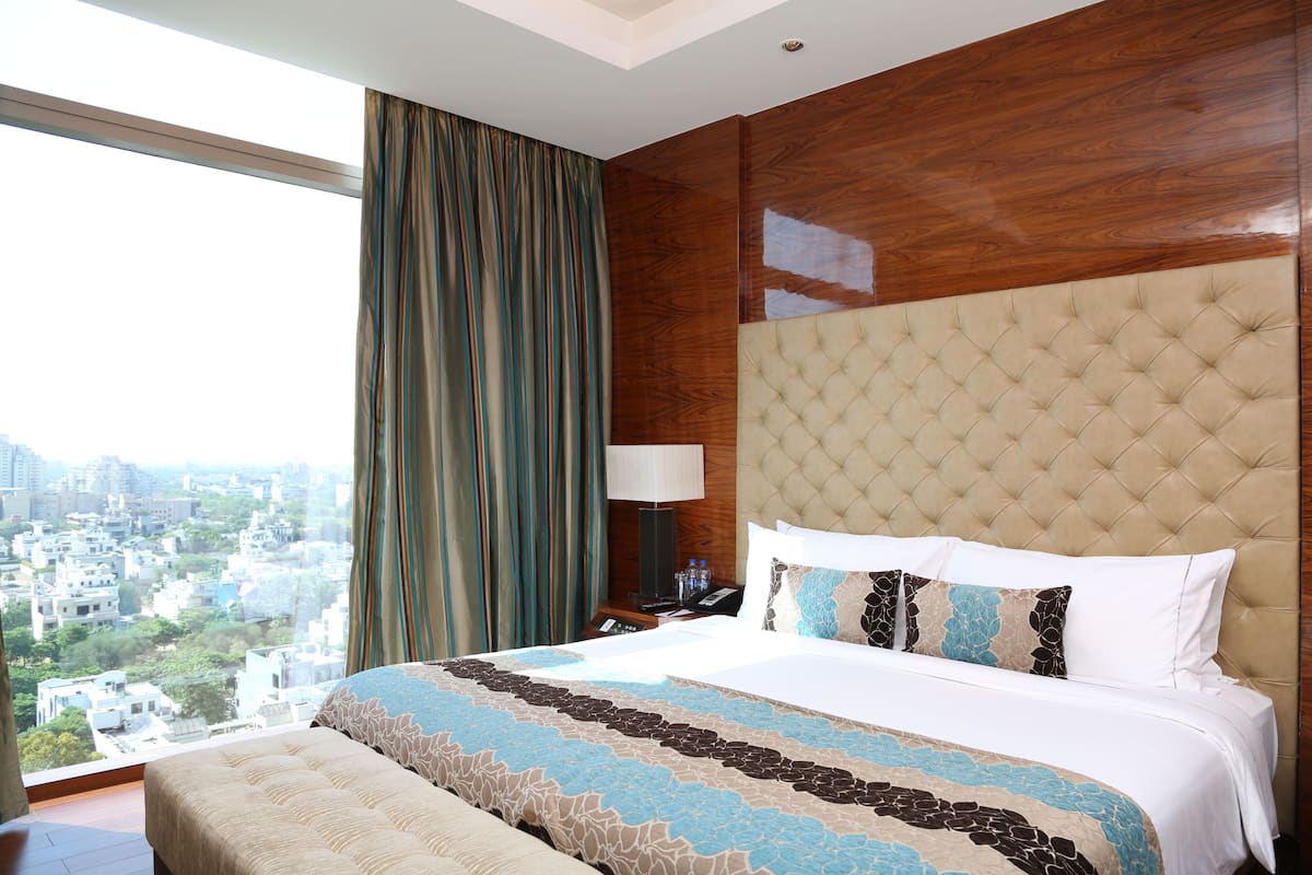A hotel room with a large bed, a view of the city, and a wooden headboard.