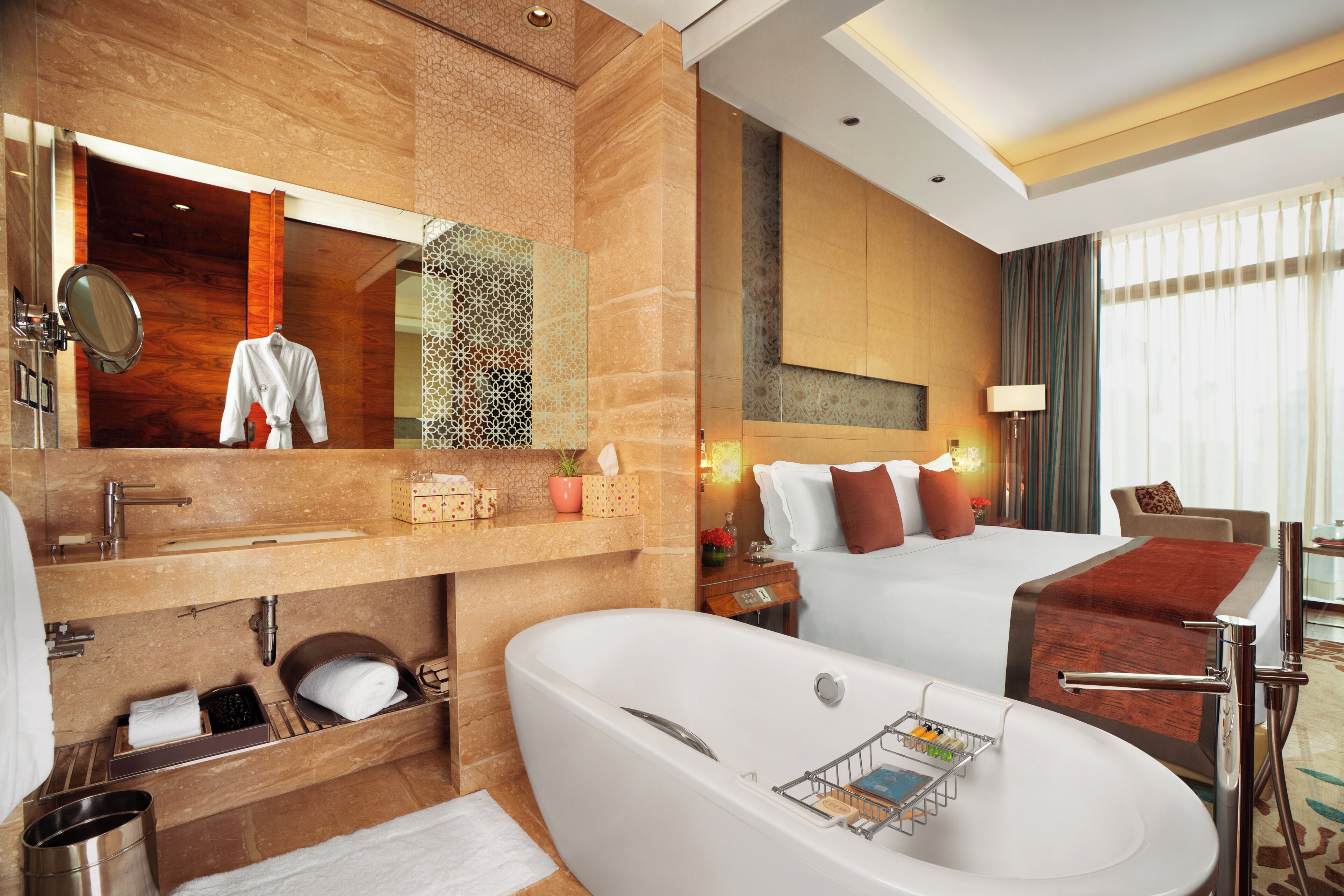 Una habitación de hotel moderna con una cama grande, baño separado con bañera, tocador con espejo y una zona de estar con mesa y sillas.