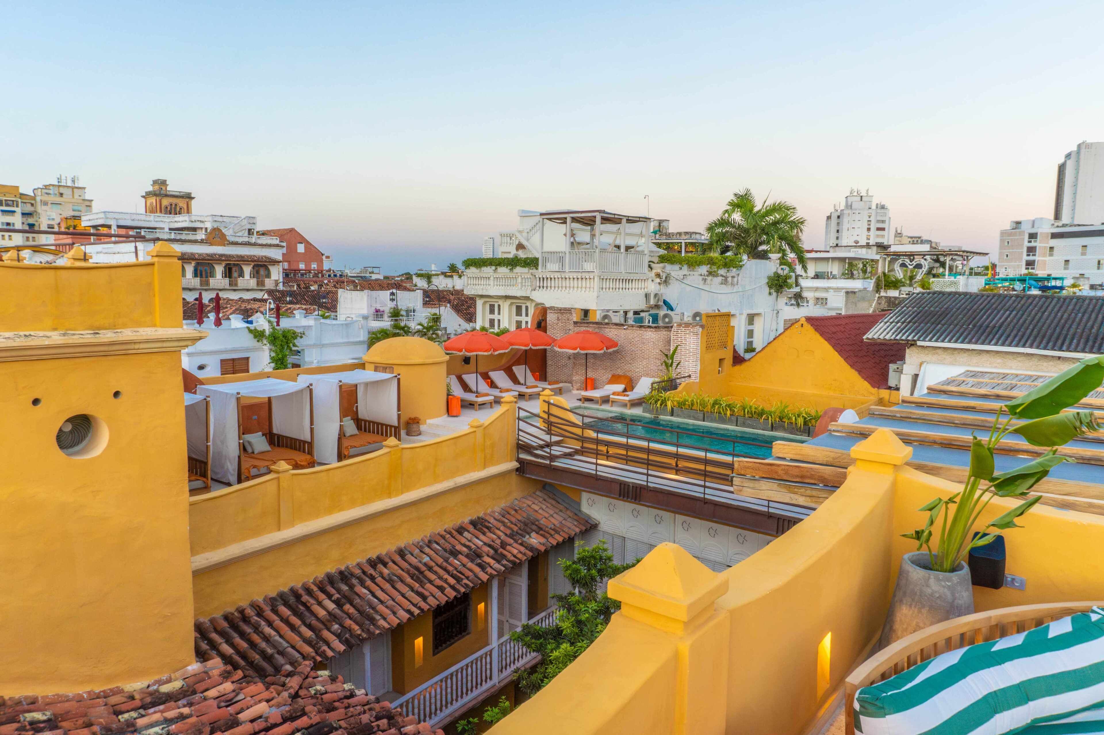 A rooftop with a swimming pool, multiple sun loungers, and a view of the cityscape.