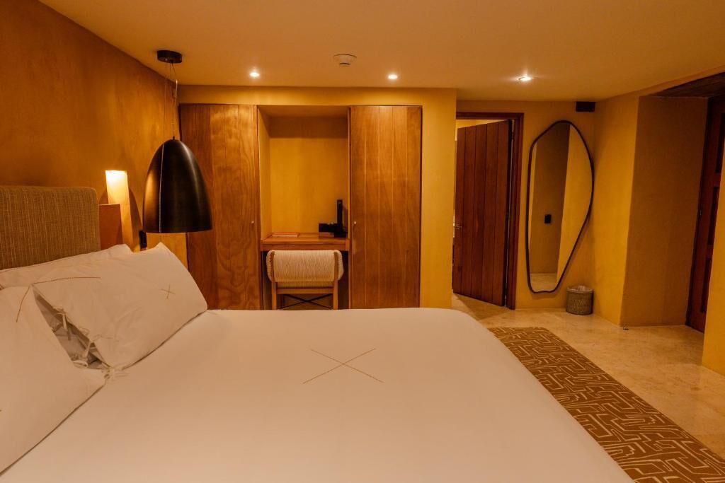Quarto de hotel com cama, escrivaninha, espelho e armário.