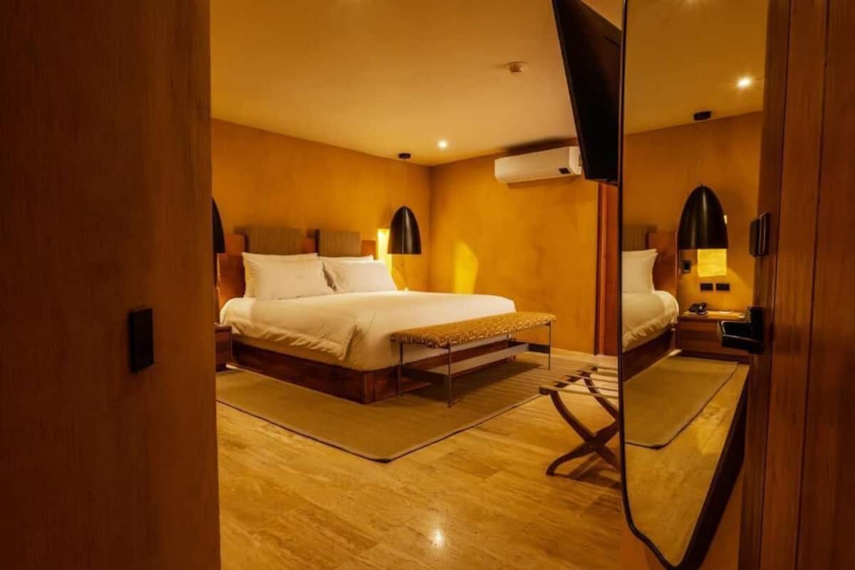 A hotel room with a bed, bedside tables, a mirror, and an air conditioning unit.