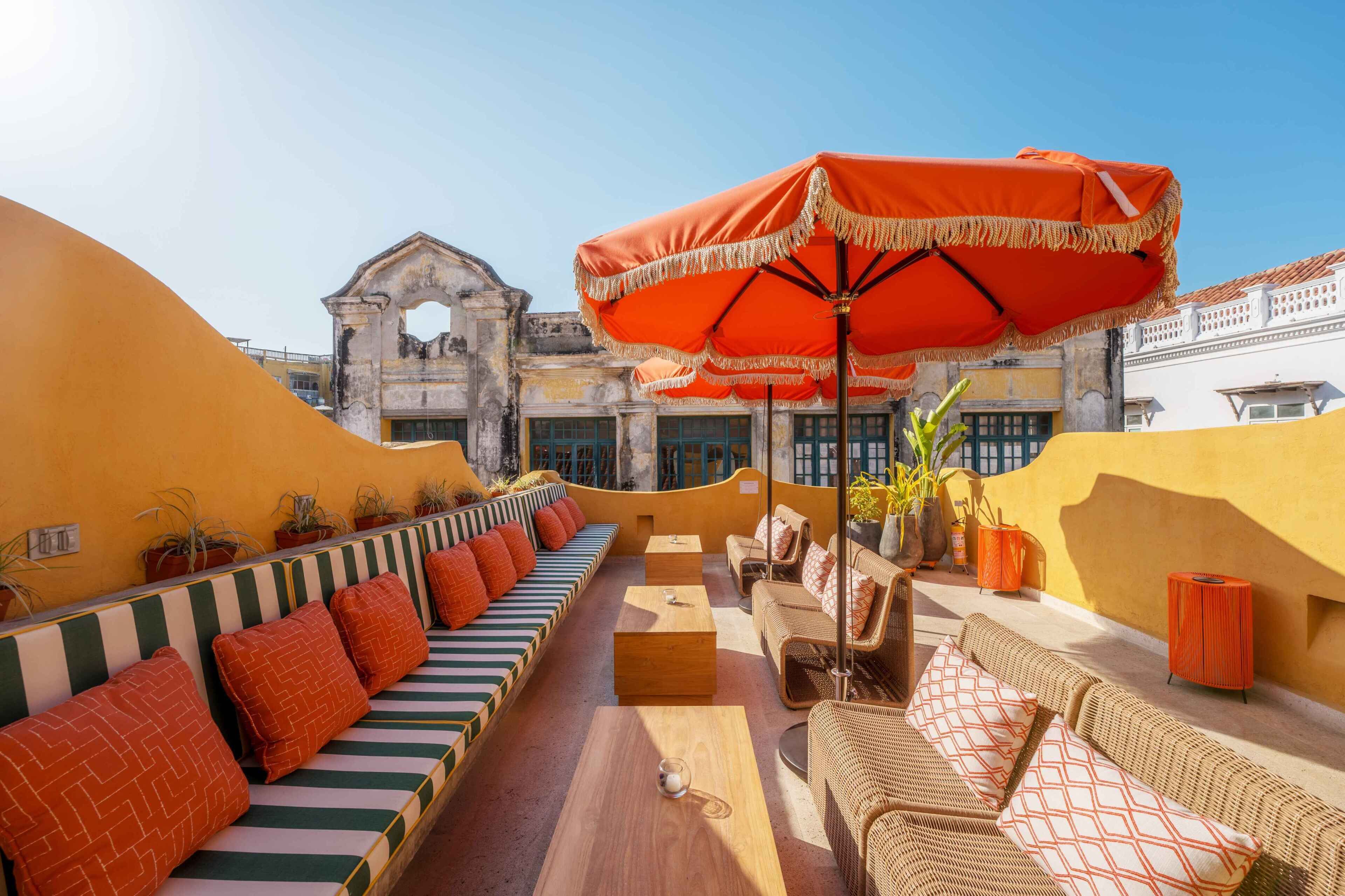 A rooftop terrace with a long bench, wicker furniture, and a large orange umbrella.