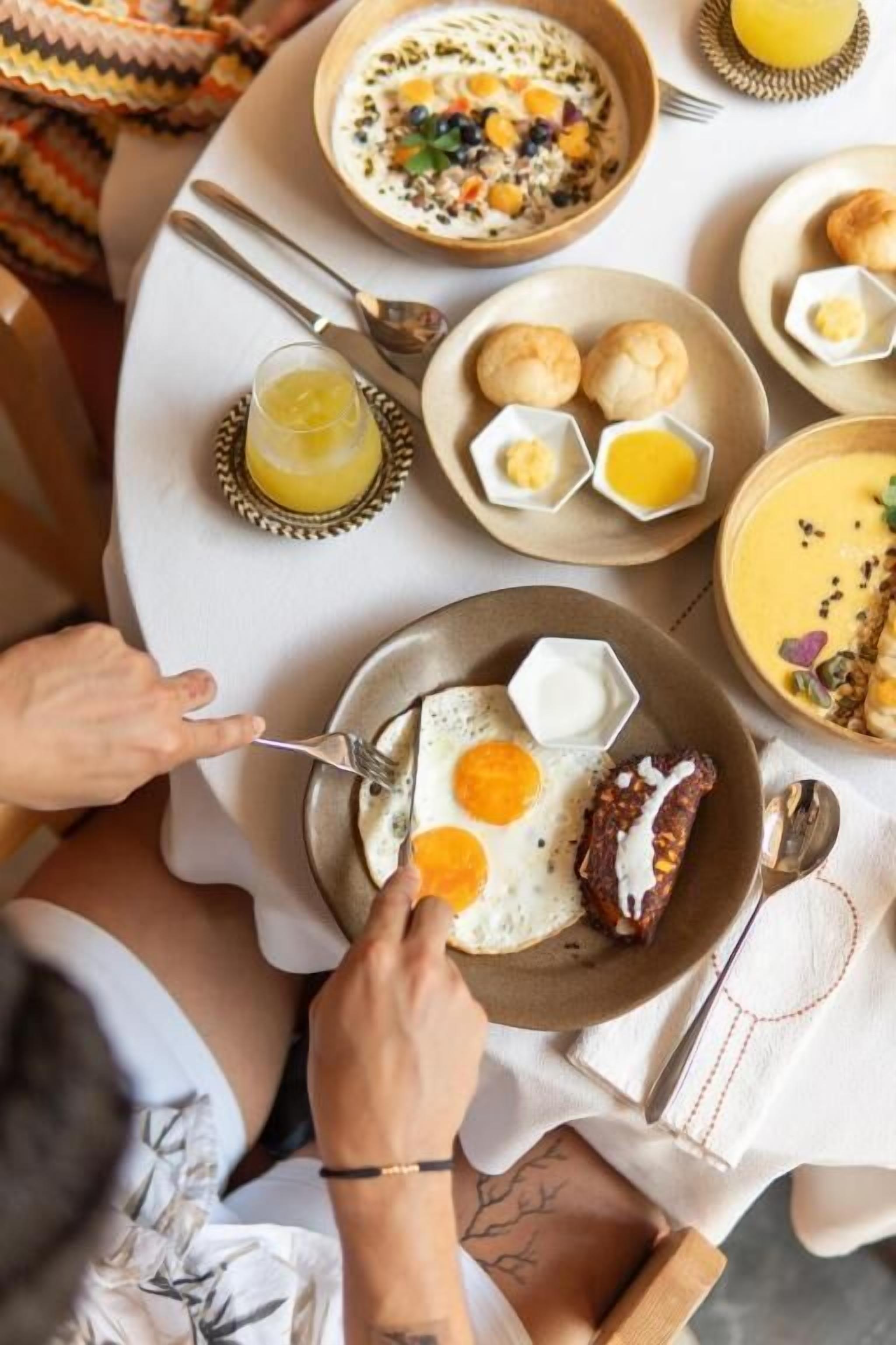 A breakfast setting with a plate of eggs, sausage, and toast, accompanied by a bowl of soup and a glass of orange juice.