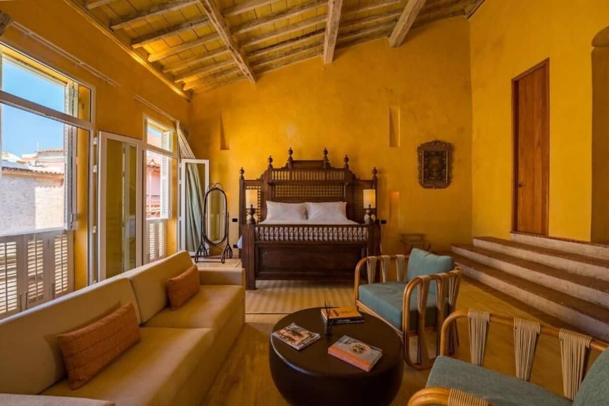 A room with a bed, sofa, and a round table with magazines.