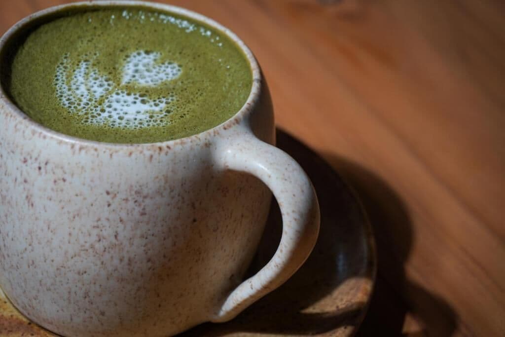 Una taza de cerámica con una bebida verde y un diseño de espuma con forma de corazón sobre un platito.