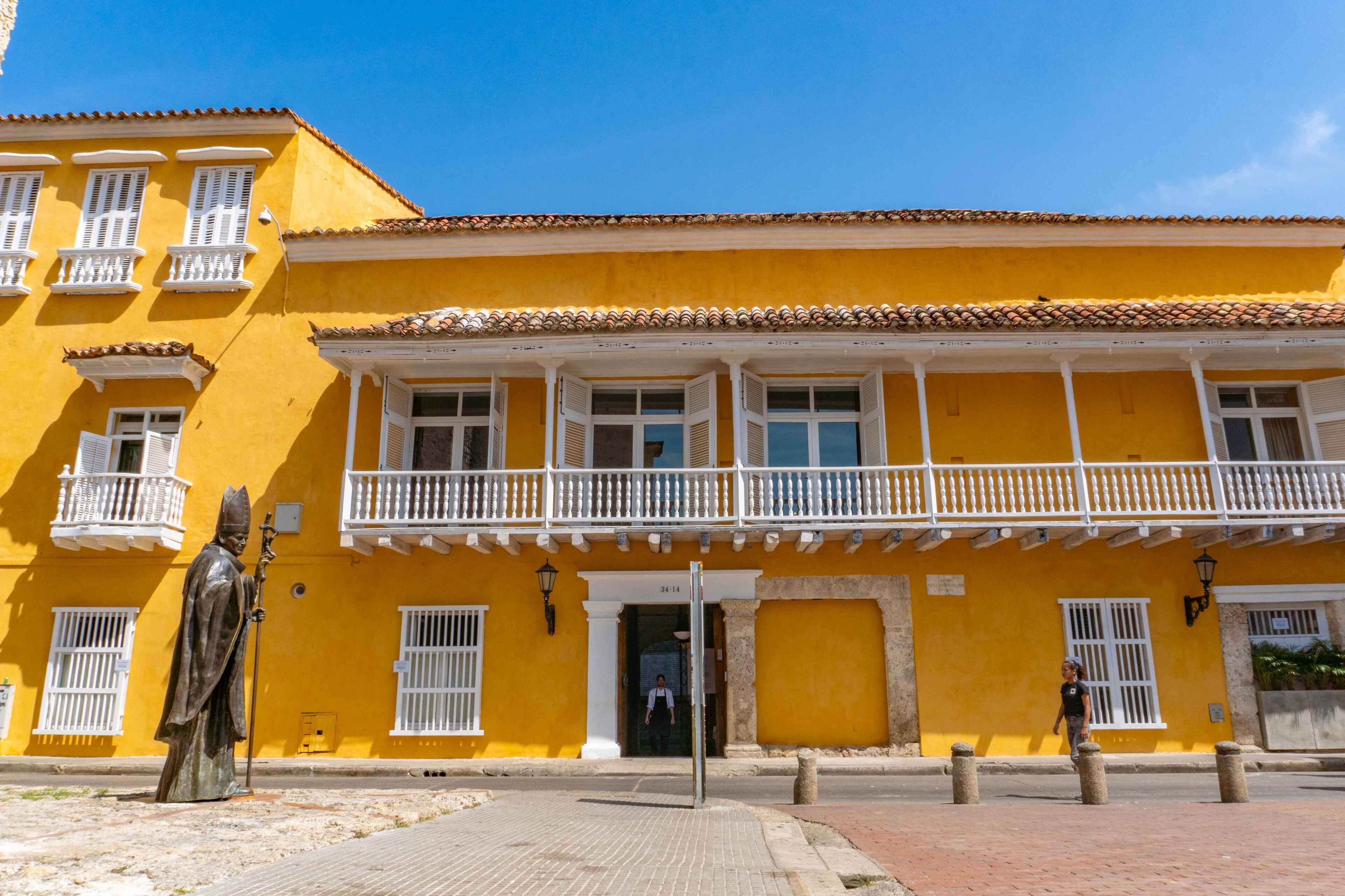 Un edificio amarillo con un balcón, una estatua y una calle en su parte frontal.