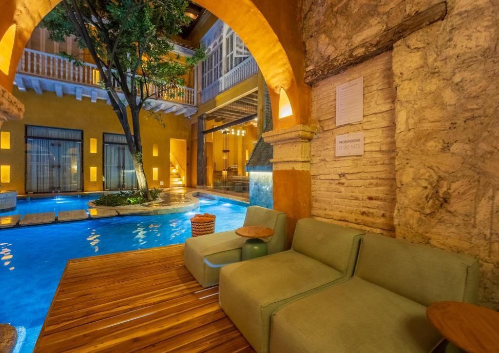 An indoor pool area with a wooden deck, green sofas, and a stone wall.