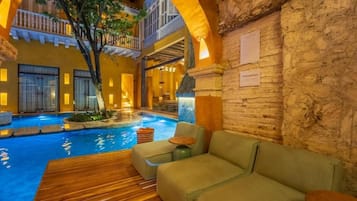 Un área de piscina interior con cubierta de madera, sofás verdes y una pared de piedra.
