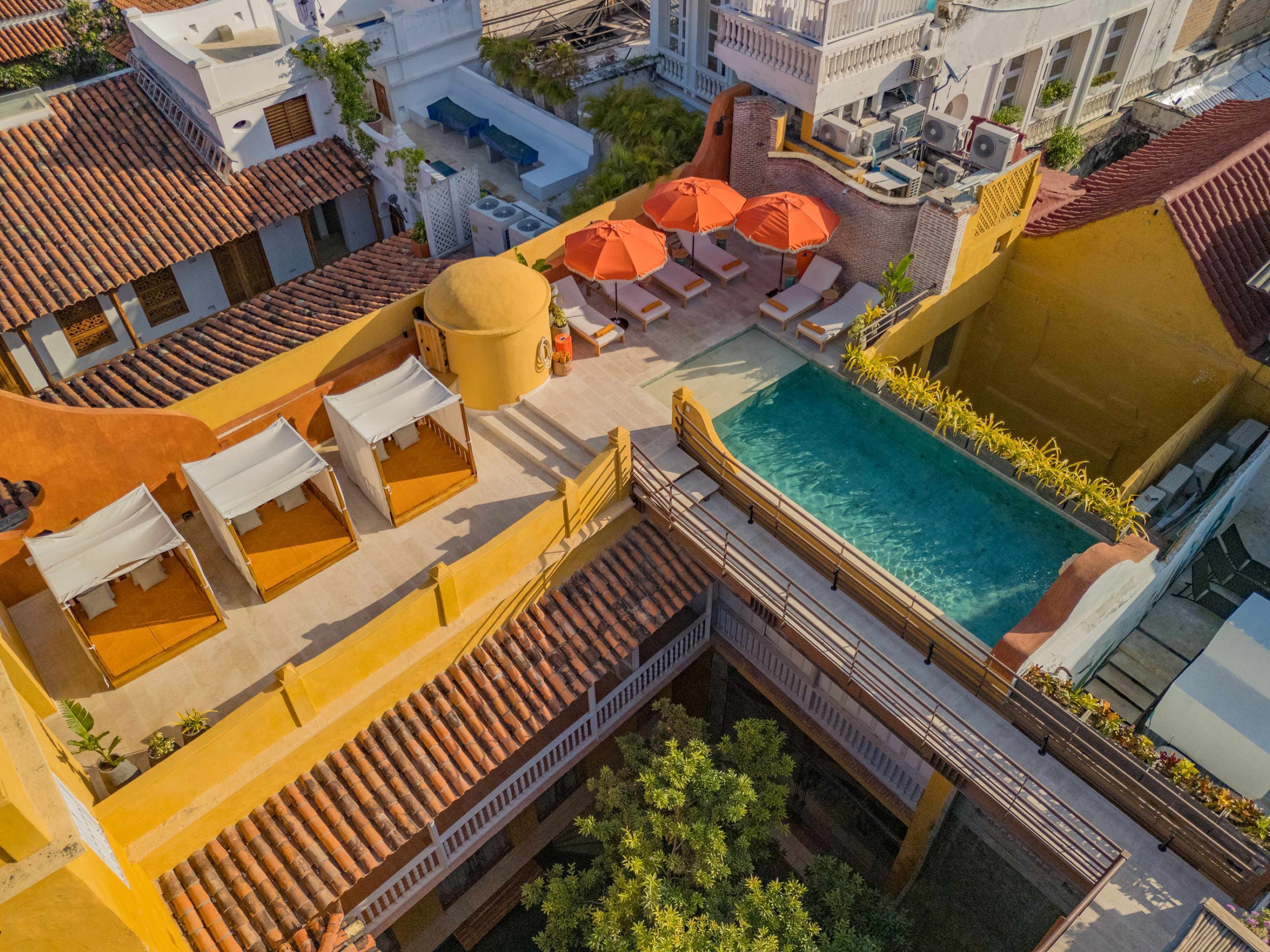 Zona de piscina en la azotea con tumbonas y sombrillas, rodeada de edificios con tejados de teja.