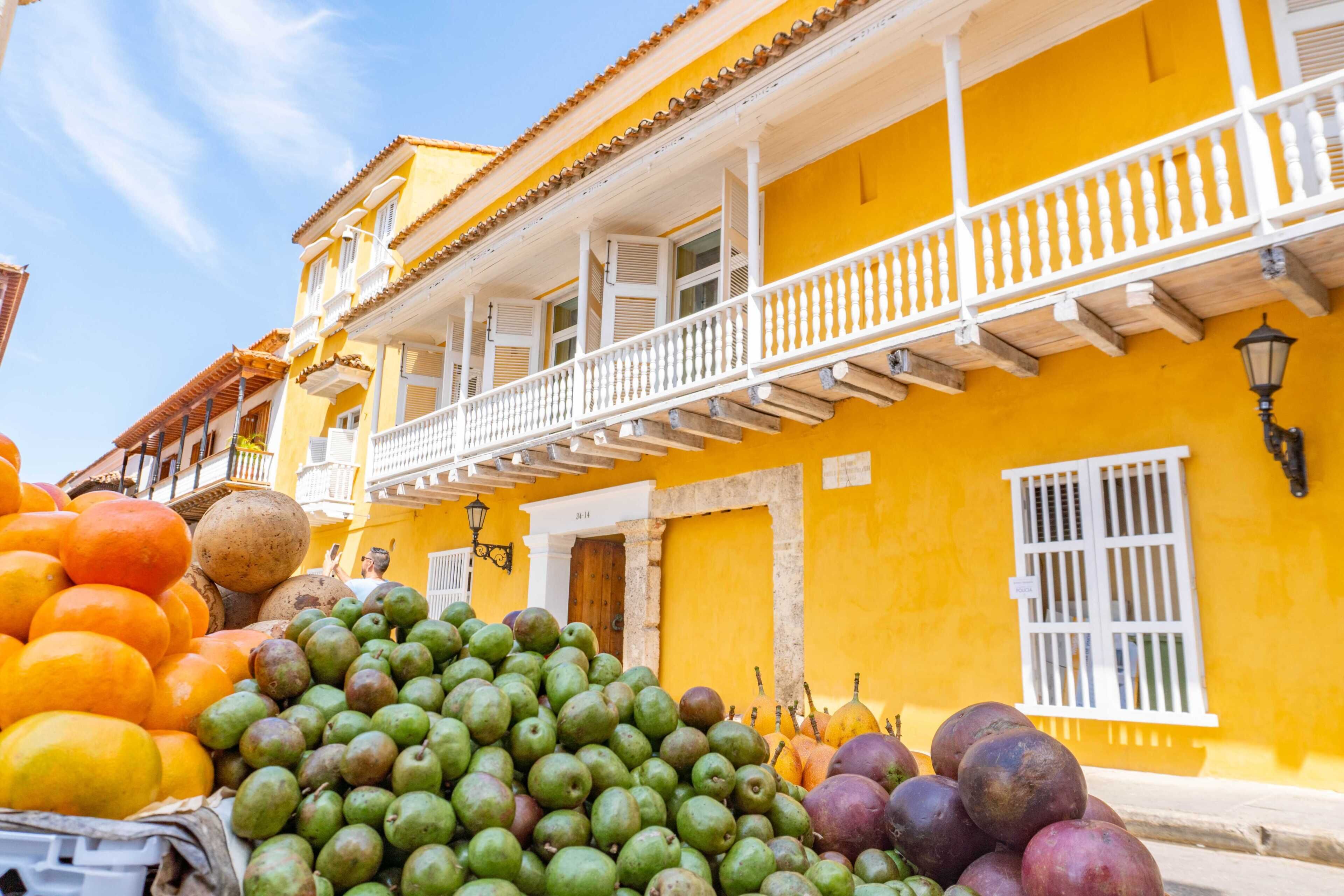 Un bâtiment jaune avec un balcon et un étal de fruits devant.
