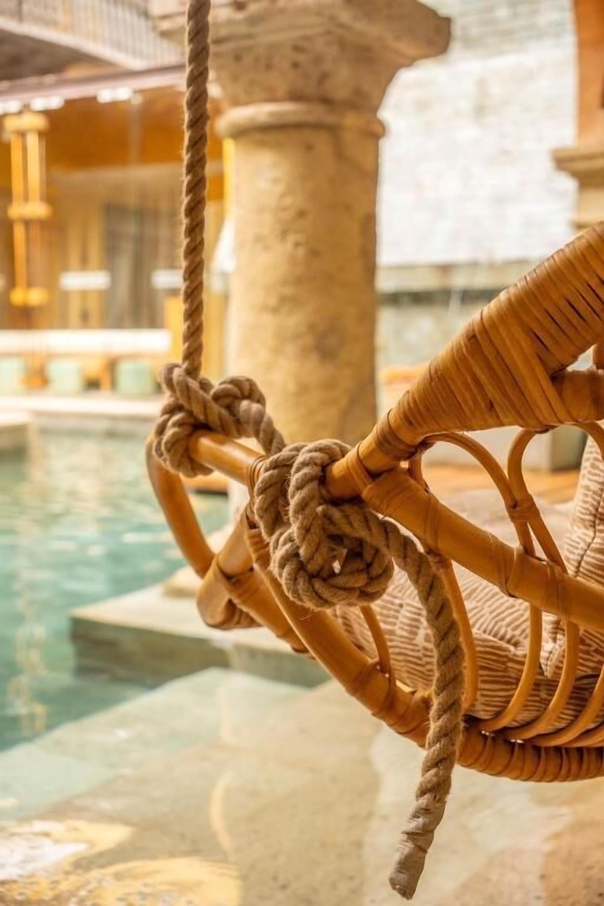 Una silla de mimbre con cuerdas alrededor, ubicada cerca de una piscina con columnas de piedra y una vista despejada del agua.
