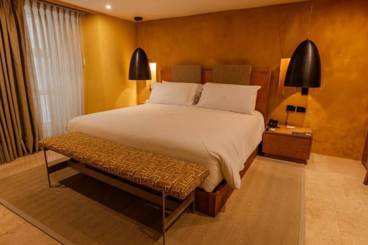 A hotel room with a bed, bedside tables, a bench, curtains, and wall-mounted lamps.