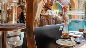 Ein Barista bereitet ein Getränk an einem Tresen zu, mit Blick auf einen Außenpool und eine Treppe.