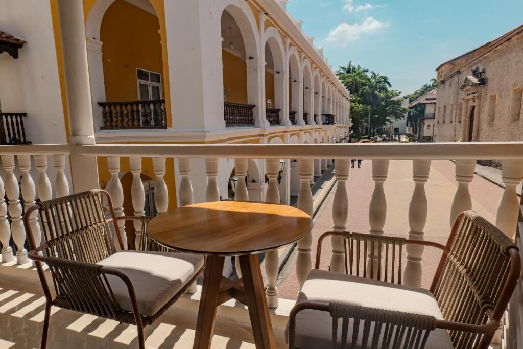 A balcony with two wicker chairs and a small round table, overlooking a street with historic buildings.