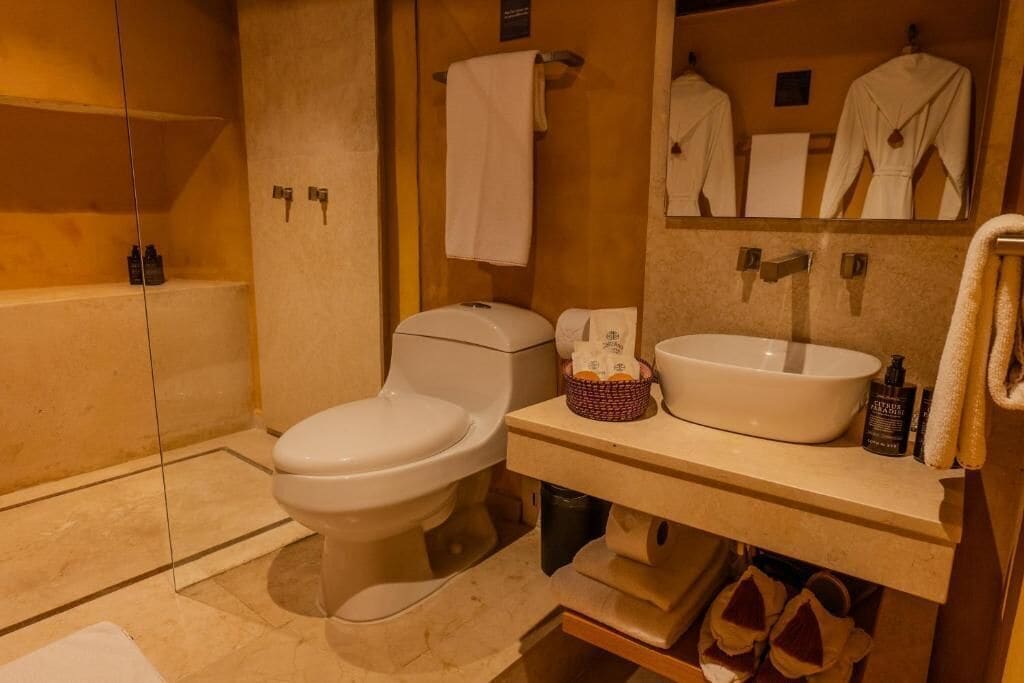 A bathroom with a toilet, sink, and mirror. There are towels and toiletries on the counter.