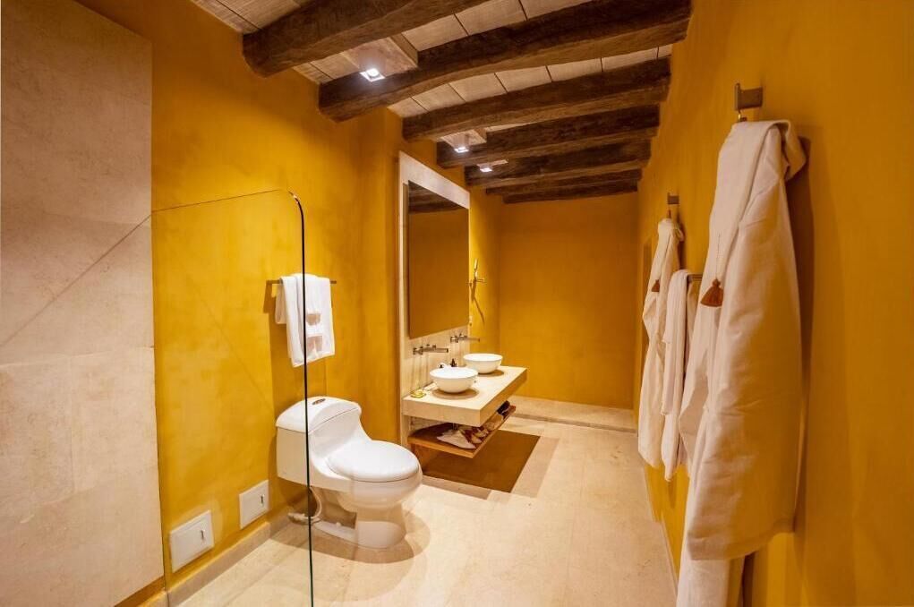 A bathroom with a toilet, two sinks, a mirror, and towels on a rack.