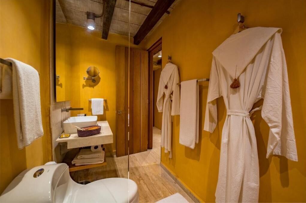 Une salle de bain avec un plancher en bois, un lavabo blanc, un miroir, ainsi que plusieurs serviettes et peignoirs blancs accrochés au mur.