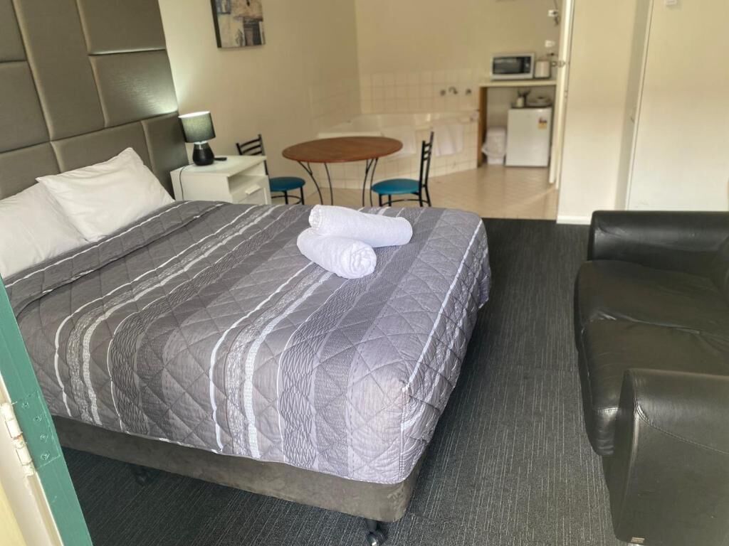 Ein Hotelzimmer mit einem Bett, einem kleinen Tisch, einem Sessel, einer Couch und einer Küchenzeile im Hintergrund.