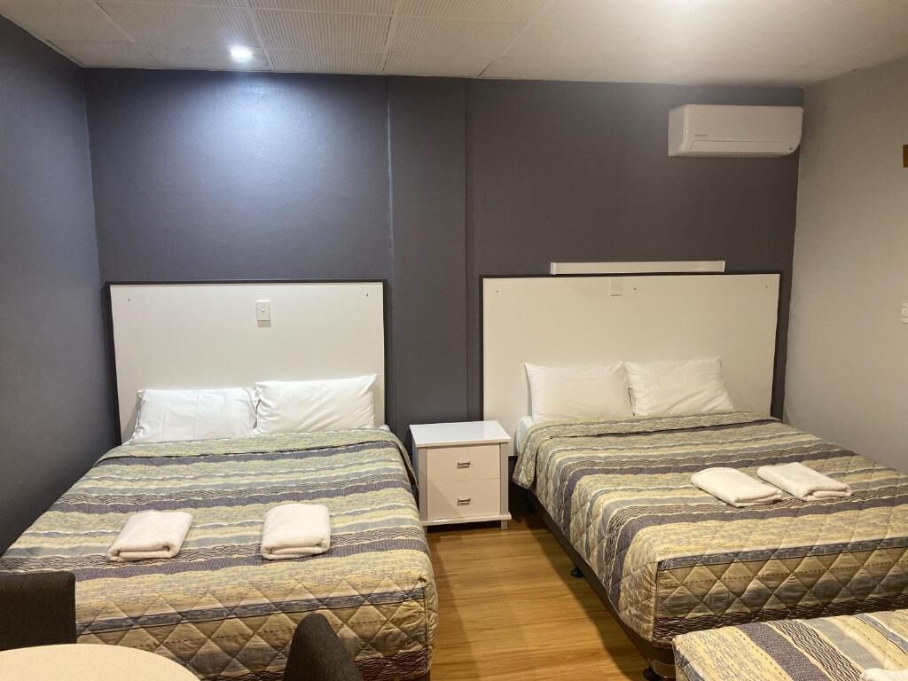 A hotel room with two single beds, a small bedside table with drawers, and a wall-mounted air conditioning unit.