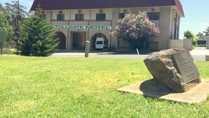Un edificio con un letrero que dice 'Tollgate Motel', con techo rojo, un gran arbusto y un monumento de piedra al frente.