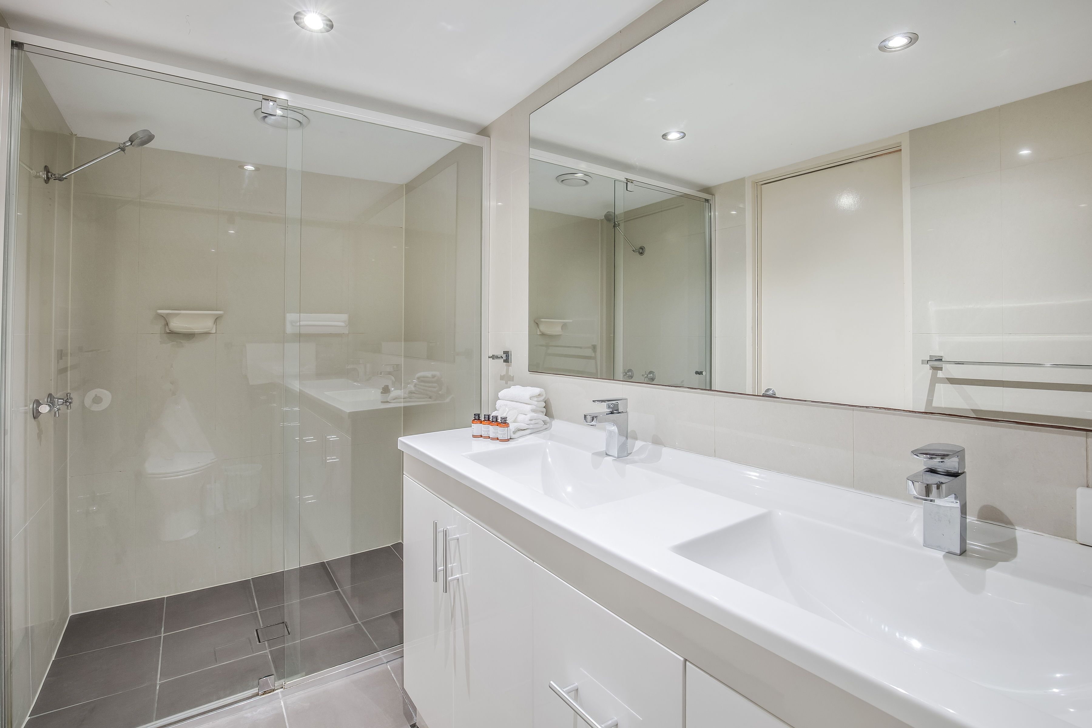 A modern bathroom with a glass-enclosed shower, a large white sink, and a mirror above the sink.
