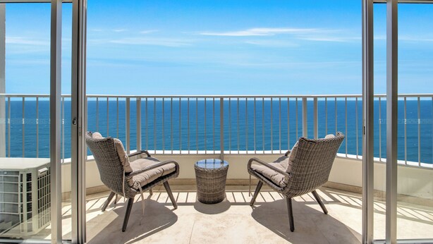 Un balcone con due poltrone in vimini e un tavolino, con vista su un mare azzurro e limpido.