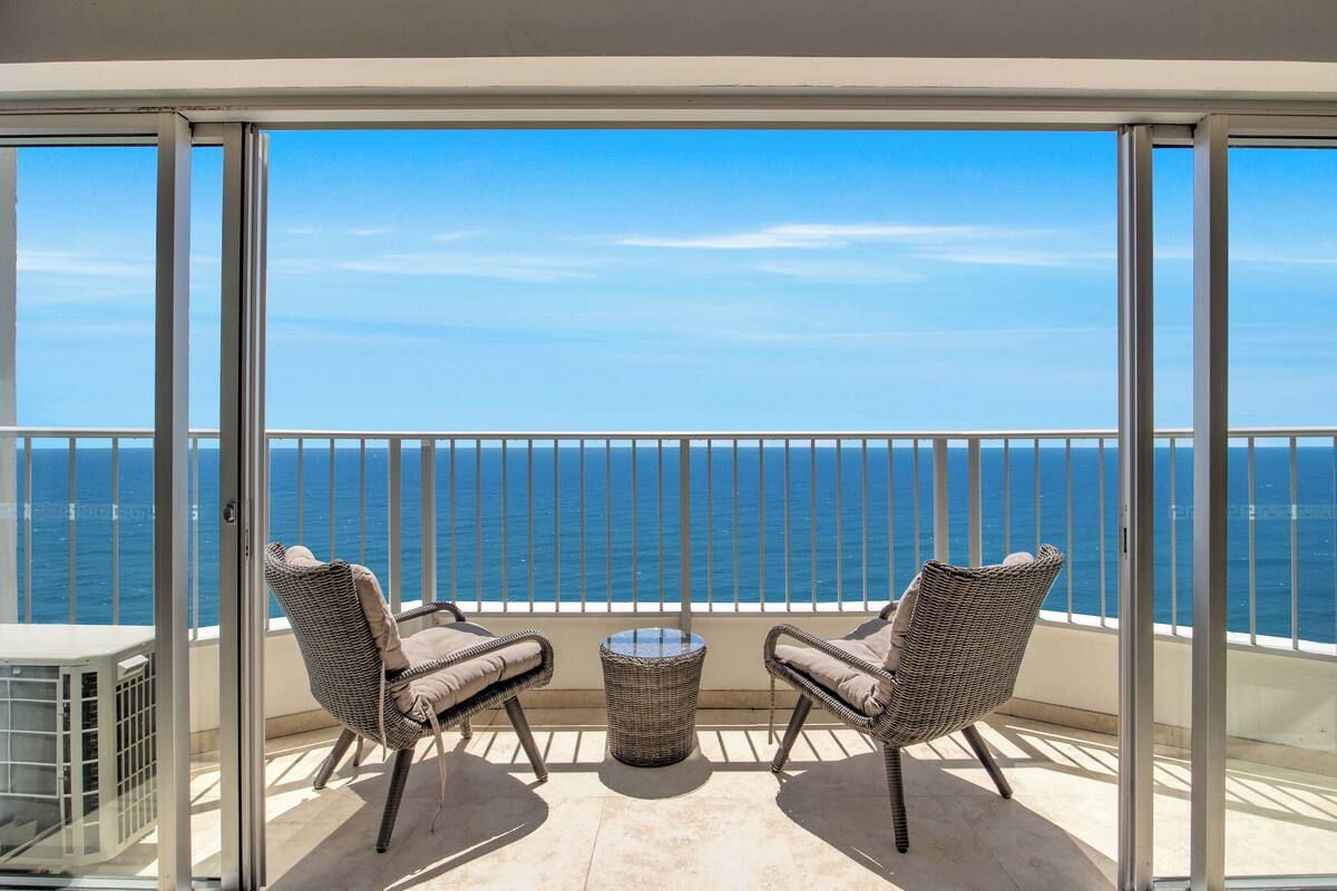 A balcony with two wicker chairs and a small table, overlooking a clear blue sea.