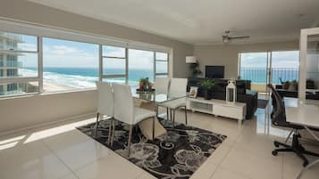 Un salón moderno con un ventanal grande con vistas al océano, una mesa de comedor de vidrio, un sofá y un televisor.