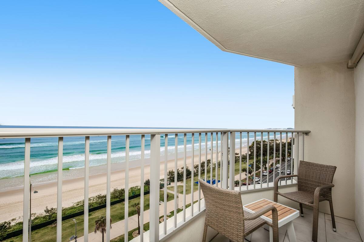 A balcony with wicker furniture overlooking a beach.