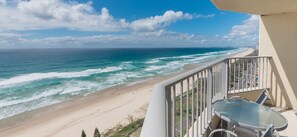 A balcony with a glass table and chairs overlooking a beach with waves and a clear sky. - Pacific Plaza Apartments (Surfers Paradise)