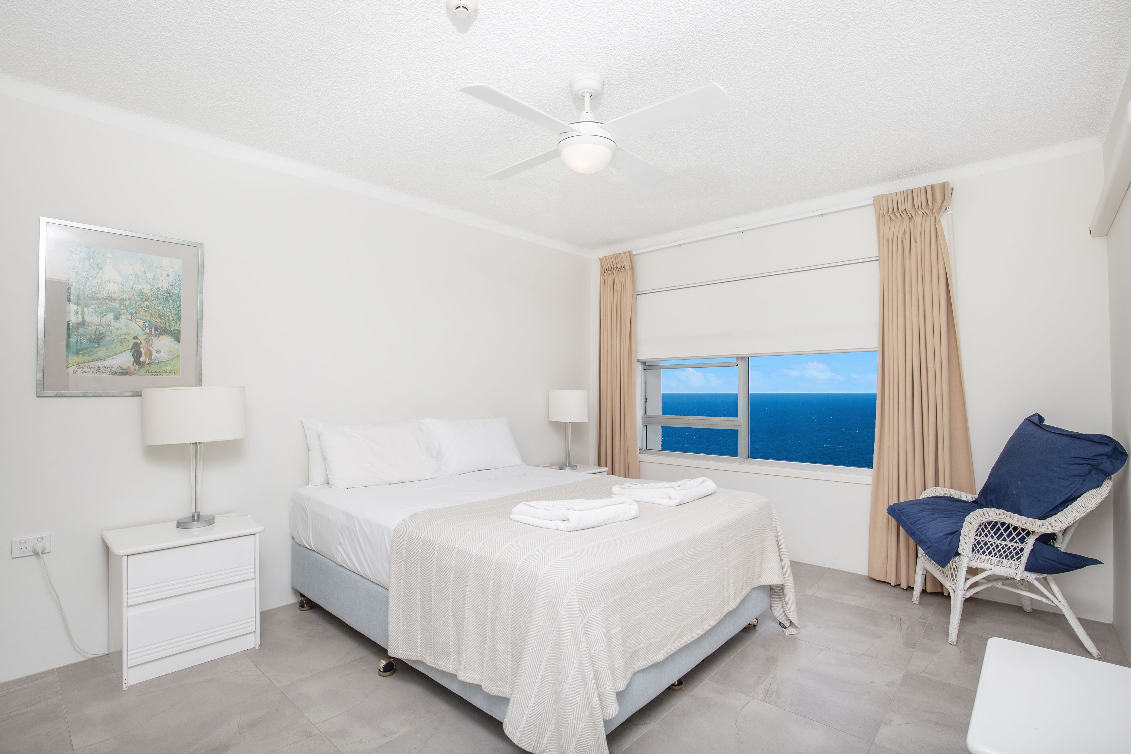 A bedroom with a bed, a chair, a window with curtains, and a ceiling fan.