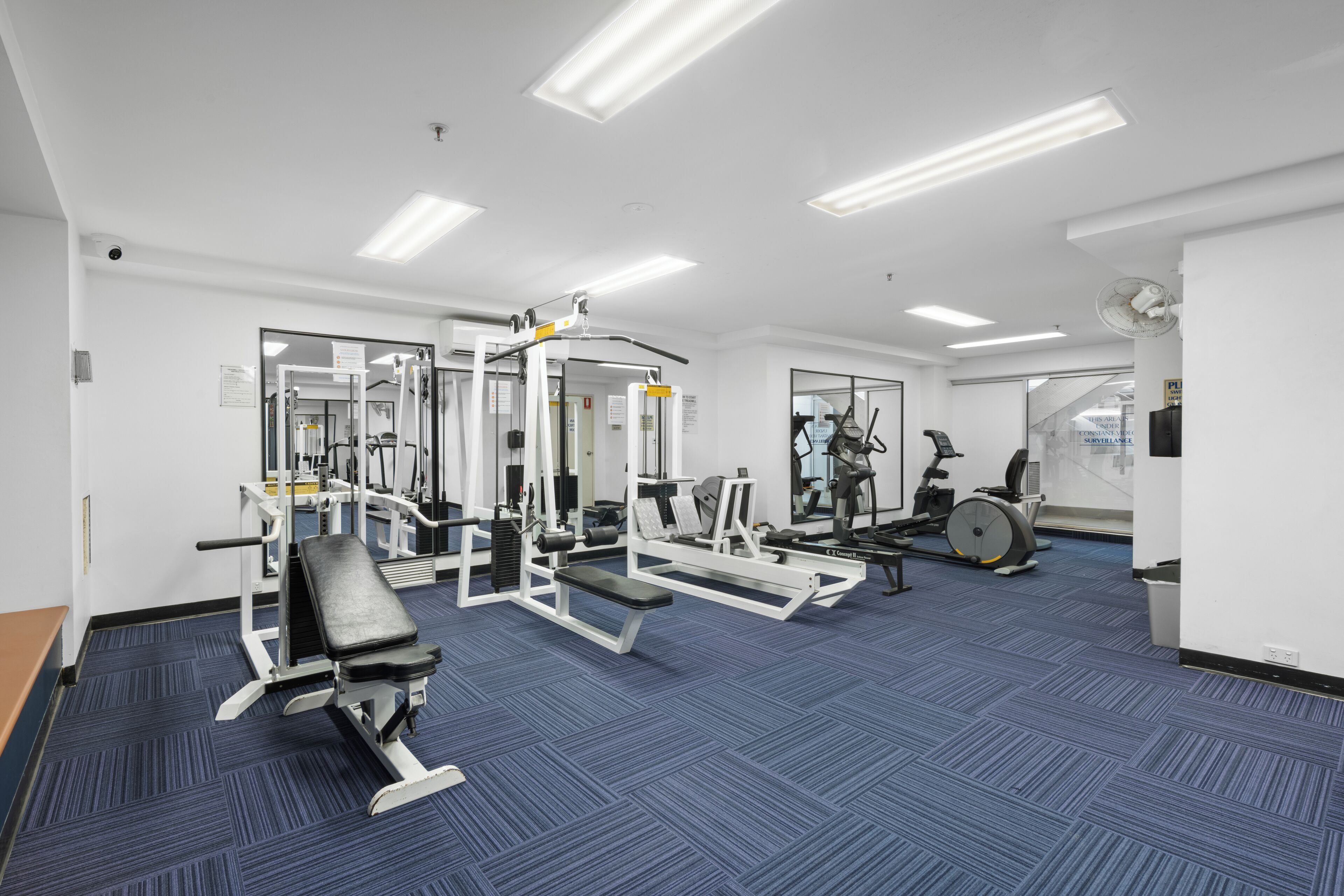 Un gimnasio con varios equipos de ejercicio, como una prensa de banca, máquinas de pesas y una elíptica.