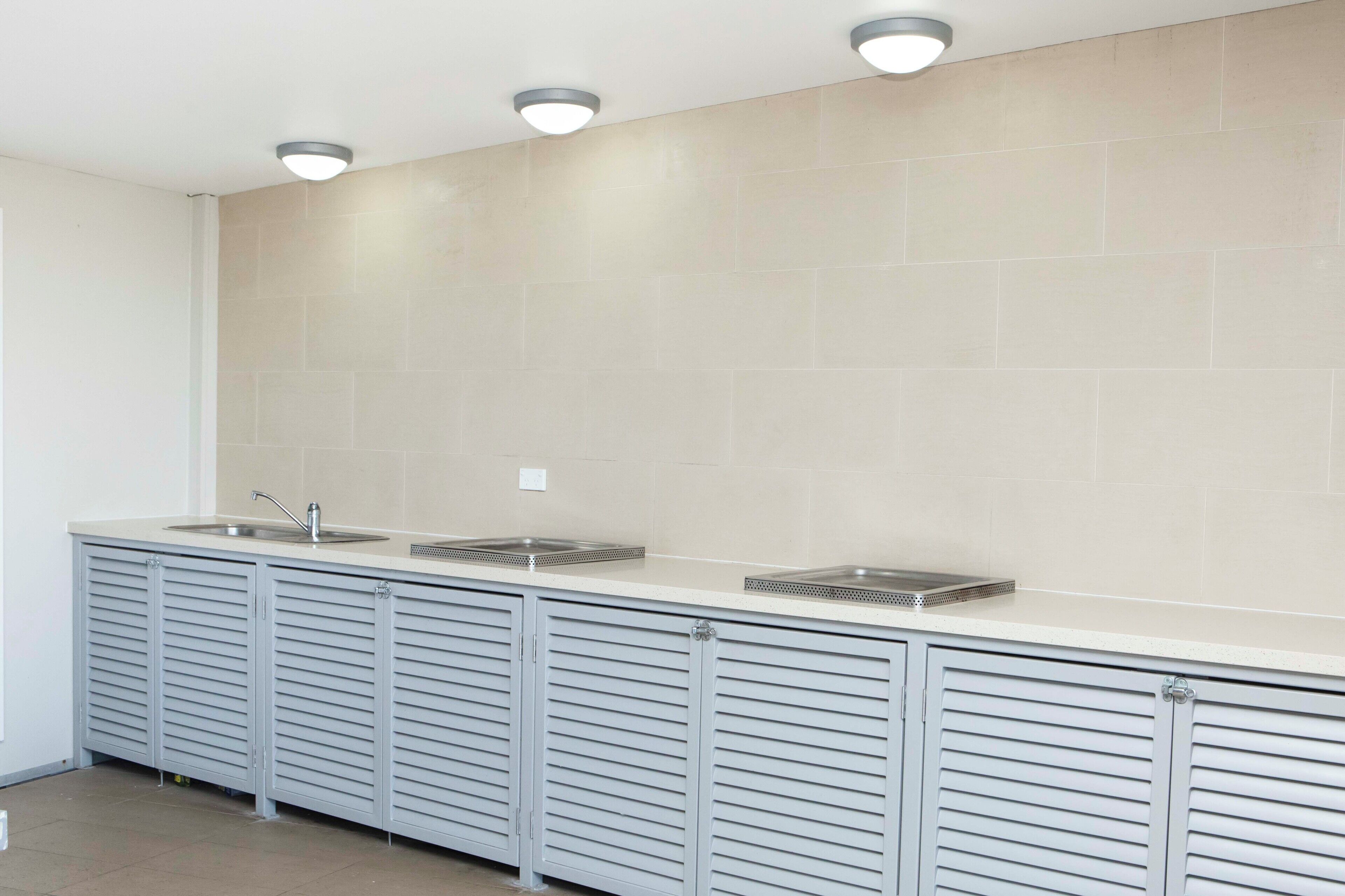 A modern kitchen with three sinks, a countertop, and overhead lighting.