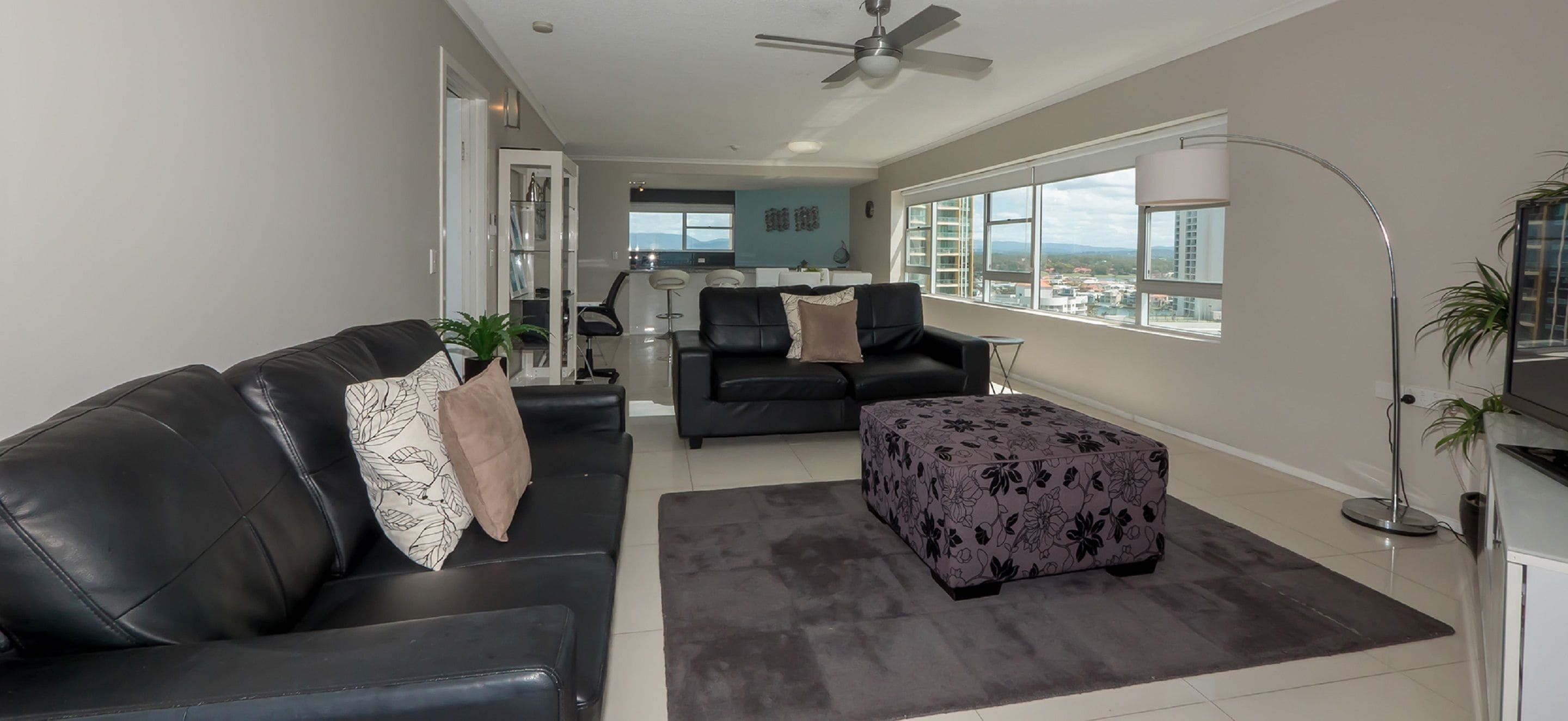 A modern living room with a sofa, ottoman, and a dining area in the background.