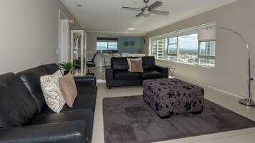 A modern living room with a sofa, ottoman, and a dining area in the background.