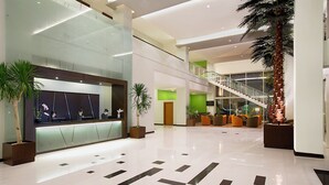 A modern lobby with a reception desk, seating area, staircase, and potted plants. - Hotel Santika Palu (Palu)