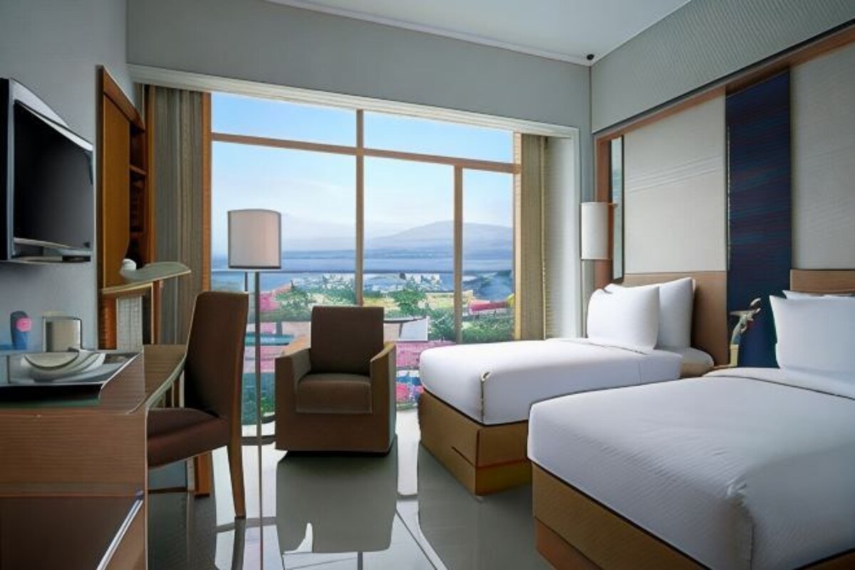 Habitación de hotel con escritorio, dos camas, una silla, televisión y ventana grande con vistas.