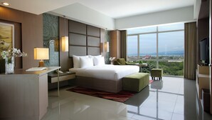 A modern hotel room with a large bed, a desk, a television, and a view of the city. - Hotel Santika Palu (Palu)