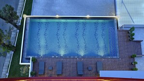 Vue aérienne d’une piscine dont le fond est recouvert de carreaux formant un motif, entourée d’une terrasse en bois et agrémentée de quelques plantes en pot.