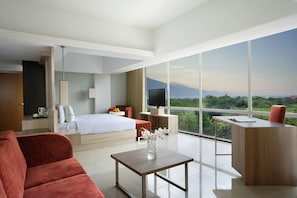 A modern hotel room with a large bed, a desk, a sofa, and a view of the mountains. - Hotel Santika Palu (Palu)