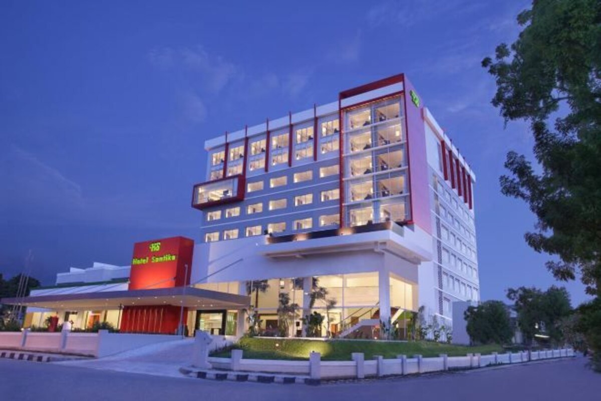 Un hotel moderno con una fachada destacada de color rojo y blanco, varios pisos y un área de entrada bien iluminada.