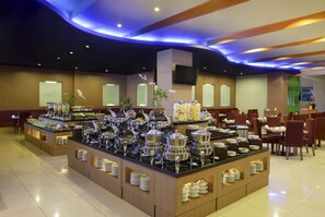 A buffet area with multiple serving stations, a flat-screen TV mounted on the wall, and a variety of dishes and utensils. - Hotel Santika Palu (Palu)