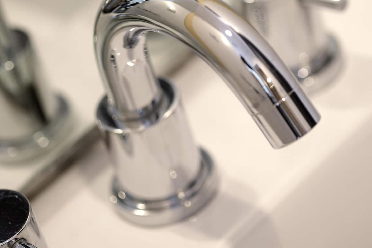 Ein chromfarbener Wasserhahn mit gebogenem Auslauf, ein Waschbecken und ein Spiegel.