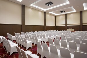 A conference room with rows of white chairs and tables, a carpeted floor, and a ceiling with recessed lighting. - Hotel Santika Palu (Palu)